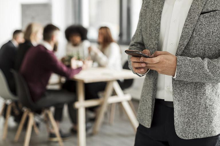Photo illustrant un homme sur son smartphone lors d'une réunion
