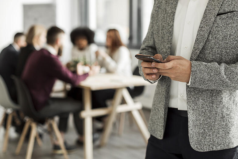 Photo illustrant un homme sur son smartphone lors d'une réunion